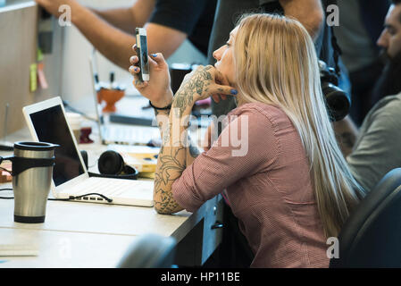 Junge Frau starrte auf Smartphone im Büro Stockfoto