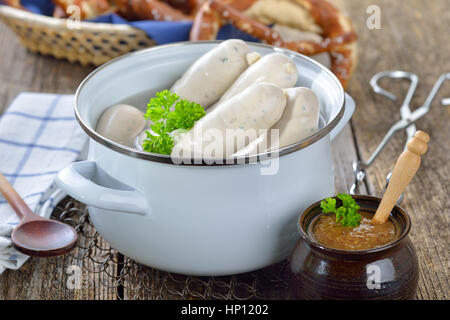 Heißen bayrische Weißwürste in einem Kochtopf Emaille auf einem Holztisch mit frischen Brezeln und süßem Senf serviert Stockfoto