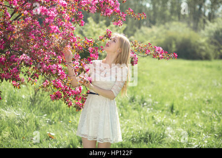 Schöne junge Mädchen im weißen Kleid genießen warme Tag im Park während der Kirschblüte an einem schönen Frühlingstag Stockfoto