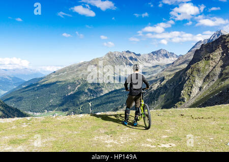 Mountainbiker steht am Rand eines Gipfels und genießt die Aussicht auf die Alpen Stockfoto
