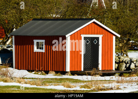 Rot, weiß und Schwarz hölzernen Schuppen im zeitigen Frühjahr mit etwas Schnee noch sichtbar auf dem Boden. Stockfoto