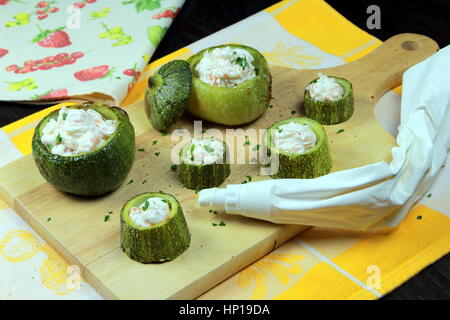 Lachs-Creme gefüllte Zucchini (Zucchini) auf einem Holzbrett mit Spritzbeutel - Gemüse und Meeresfrüchte Rezept Stockfoto