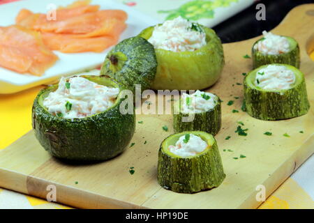 Lachs Creme gefüllte Zucchini (Zucchini) auf ein Holzbrett - Bokeh Räucherlachs im Hintergrund - Gemüse und Meeresfrüchte Rezept Stockfoto
