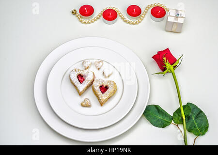 Linzer Mandel Cookies auf weißen Teller in Herzform. Romantische Einrichtung rote Rosen und Kerze leuchtet Ffor Jubiläum, Hochzeit, Valentinstag-Konzept Stockfoto