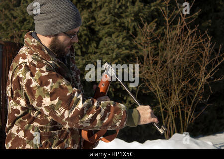 Mann im Winterwald lädt pneumatische Waffen.  Hunter gekleidet in Camouflage mit Druckluftpistole, Gewehr Stockfoto