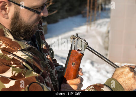 Mann im Winterwald lädt pneumatische Waffen.  Hunter gekleidet in Camouflage mit Druckluftpistole, Gewehr Stockfoto