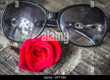 Damen Sonnenbrillen und rote rose auf einem Holztisch liegen. Close-up. Stockfoto