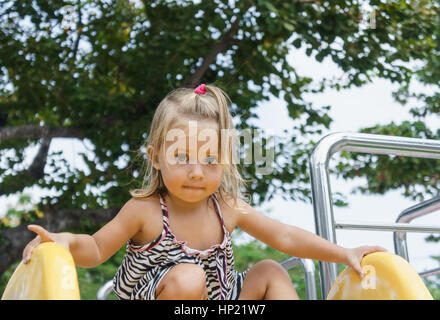 Ein wunderschönes kleines Mädchen gilt für eine Fahrt auf einem Kinder-Hügel. Hitze des Sommers. Spielplatz Stockfoto