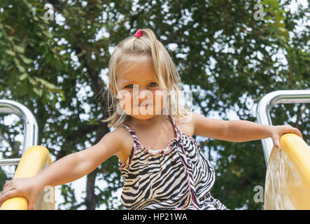 Ein wunderschönes kleines Mädchen gilt für eine Fahrt auf einem Kinder-Hügel. Hitze des Sommers. Spielplatz Stockfoto