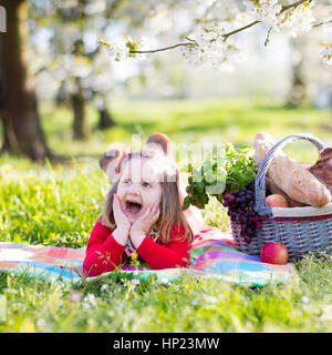 Meine lieben Kinder, Essen im Freien. Kinder mit Picknick-Korb im Frühlingsgarten mit blühenden Apfel- und Kirschbäumen Baum. Entspannen Sie sich auf Colo Vorschulkind Mädchen Stockfoto