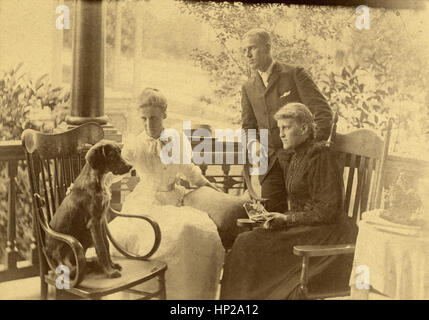 Antike c1890 Foto, Gruppe von viktorianischen Erwachsenen auf Veranda mit Hund. Ort: New England, USA. QUELLE: ORIGINAL FOTOABZUG. Stockfoto