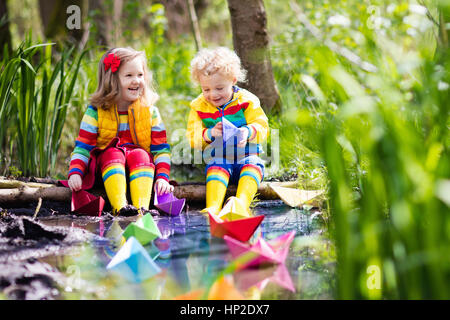Kinder spielen mit bunten Papierschiffchen in einem kleinen Fluss an einem sonnigen Frühlingstag. Kinder spielen, die Natur zu erforschen. Bruder und Schwester, die Spaß an einem Stockfoto