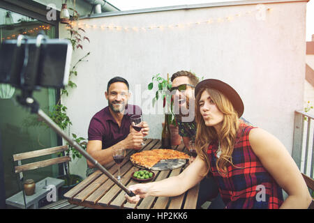 Drei junge attraktive europäische Freunde mit großen Pizza posiert für die Kamera-Handy auf Selfie zusammen am Tisch sitzen bleiben Stockfoto