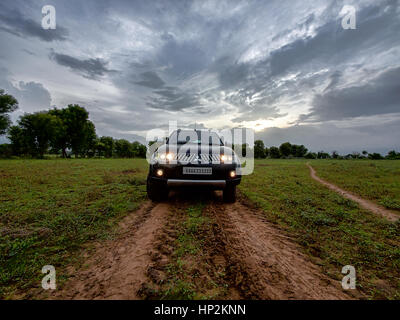 Ein schwarzer Mitsubishi Pajero Sport SUV-Fahrzeug in ein grünes Feld mit Wanderwegen, Lichter auf, dramatische Wolken im Himmel Stockfoto