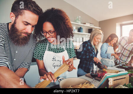 Gemischte Gruppe von guten Freunden vorbereiten pasta Dinner in der Küche zusammen. Rezeptbuch auf staffelei vor Ihnen. Stockfoto