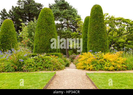 Stein Weg Kreuzung Sommer Blumen, Blumenbeete und Rasen in einem angelegten Garten mit Pinien und geformte Koniferen Stockfoto