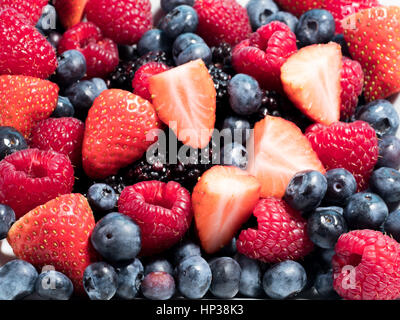 Gemischte Winter Früchte von Heidelbeeren, Himbeeren, Blackberrys und Obstüberguss in eine Schüssel weiß auf blauem Hintergrund Stockfoto