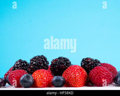 Gemischte Winter Früchte von Heidelbeeren, Himbeeren, Blackberrys und Obstüberguss in eine Schüssel weiß auf blauem Hintergrund Stockfoto