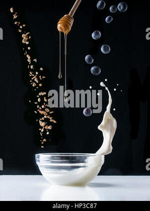 Fallende Müsli mit Milch Spritzen, Heidelbeeren und Honig fließt vom Wagen fallen. Gesundes Frühstückszutaten. Fliegendes Essen Stockfoto