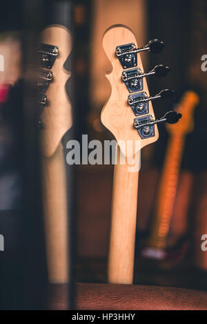 Detail der Bass-Gitarre Kopf und Hals mit Reflexion. Anderen Gitarrenhälse im Hintergrund. Vintage-Filter. Bass-Gitarre Stillleben. Hintergrundmusik. Stockfoto