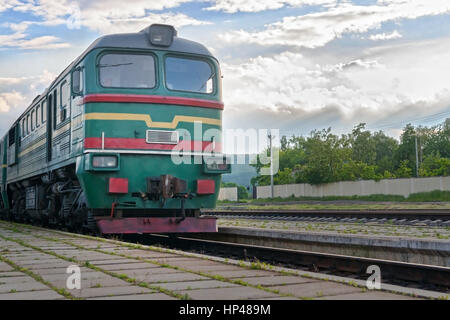 grüne Lokomotive kommt am Bahnhof auf dem Hintergrund der Gewitterhimmel. Stockfoto