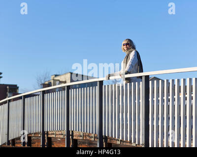 Reife Frau lehnt sich an das Geländer der Brücke, sonnigen Wintertag Stockfoto