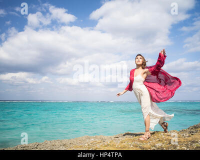 Junge Frau an der Küste direkt am Meer tragen Kleid und roten Schal in Motobu, Okinawa, Japan Stockfoto