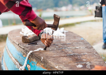 Nepali Mann repariert ein Ruderboot die traditionelle Art, mit Baumwoll-Seil und Teer Stockfoto