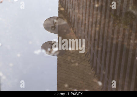 Reflexion in Pfütze von Mauer, Zaun und Satelliten-Gerichte. Stockfoto