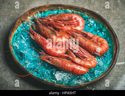 Rohe ungekochte rote Garnelen auf abgebrochene Eis in Türkis Blau Keramik Schale über graue konkreten Hintergrund, Tiefenschärfe, horizontale Komposition. Frische s Stockfoto