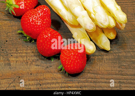 Erntefrische Spargel und Erdbeeren auf einem urigen, alten Holzbrett Stockfoto