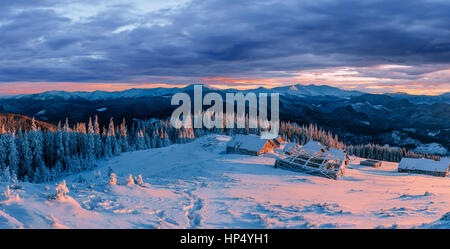 Fantastischen Sonnenuntergang über schneebedeckte Berge und Holzchalets. Stockfoto