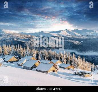 Fantastischen Sonnenuntergang über schneebedeckte Berge und Chalets aus Holz Stockfoto