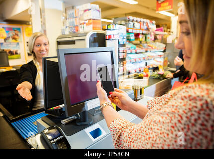 Kassierer gestikuliert während weibliche Kunde macht NFC Zahlung Stockfoto