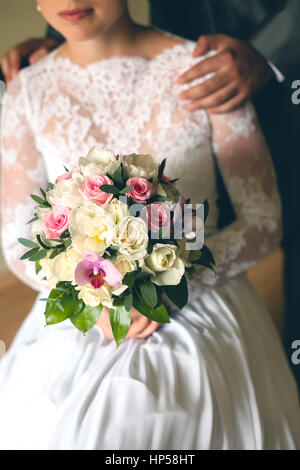 die wunderschöne Braut hält in der hand ein Brautstrauß aus Frühlingsblumen und ihrem Bräutigam hält sie sanft von einer Schulter. Der Bräutigam umarmt die Braut. Stockfoto