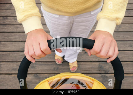 Overhead Schuss der jungen Mutter eine Kutsche spazieren. Hände halten Kinderwagen Griff. POV erschossen Stockfoto