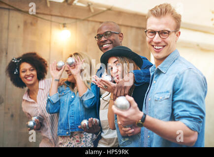 Gruppe der lächelnde Schöne junge Menschen, Männer und Frauen in Freizeitkleidung stehend innen und posieren für die Kamera halten Petanque Metallkugeln, Lachen Stockfoto