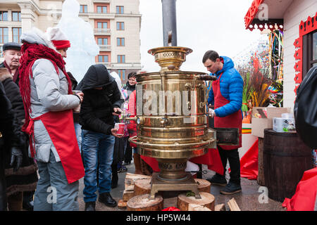 Moskau, Russland. Sonntag, 19. Februar 2017. Unbekannte Menschen machen Tee durch gießt heißes Wasser aus einem Wasserkocher russischer Holzkohle Samowar in Kunststoffkappen auf dekorierten Manege-Platz. Maslenitsa, Pfannkuchen, Käse-Tarif-Week-Festival, Karneval begann in der Stadt. Menschen genießen Straßentheater und heißen Pfannkuchen essen. Dies ist auch Abschied vom Winter-Festival. Der Tag ist Warm (+2C, über 36F) aber düster. © Alex Bilder/Alamy Live-Nachrichten Stockfoto