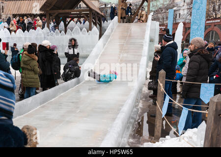 Moskau, Russland. Sonntag, 19. Februar 2017. Eis-Folie oder Eis-Lauf für Kinder durch den Schnee Festung auf Revolution Quadrat - der Hauptbereich des Festivals. Servicepersonal kümmert sich um und hilft Kindern sicher gleiten. Maslenitsa, Pfannkuchen, Käse-Tarif-Week-Festival, Karneval begann in der Stadt. Menschen genießen Straßentheater und heißen Pfannkuchen essen. Dies ist auch Abschied vom Winter-Festival. Der Tag ist Warm (+2C, über 36F) aber düster. © Alex Bilder/Alamy Live-Nachrichten Stockfoto