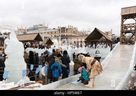 Moskau, Russland. Sonntag, 19. Februar 2017. Eis-Folie oder Eis-Lauf für Kinder durch den Schnee Festung auf Revolution Quadrat - der Hauptbereich des Festivals. Servicepersonal kümmert sich um und hilft Kindern sicher gleiten. Maslenitsa, Pfannkuchen, Käse-Tarif-Week-Festival, Karneval begann in der Stadt. Menschen genießen Straßentheater und heißen Pfannkuchen essen. Dies ist auch Abschied vom Winter-Festival. Der Tag ist Warm (+2C, über 36F) aber düster. © Alex Bilder/Alamy Live-Nachrichten Stockfoto