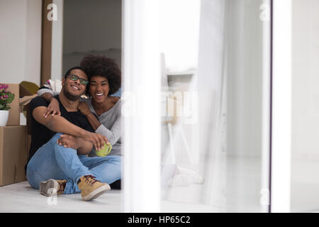 Entspannung im neuen Haus. Fröhliche junge afrikanische amerikanische paar auf dem Boden sitzen und Kaffee trinken, während Kartons herumliegen Sie Stockfoto