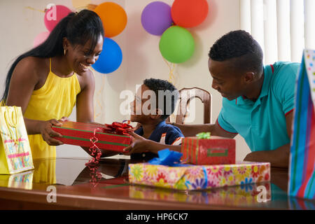 Glückliche schwarze Familie zu Hause. African american Vater, Mutter und Kind feiert Geburtstag, Spaß an der Partei. Junge Frau Geschenk Sohn zu geben. Stockfoto