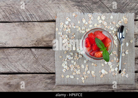 frische Erdbeeren mit Joghurt im Glas auf einem hölzernen Hintergrund. Hausgemachtes Joghurt dekoriert Minzeblätter und Beeren der Erdbeere in Glas auf vi Stockfoto