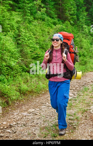 glückliche Frau Wanderer unterwegs in den Bergen wandern. Mädchen-Wanderer zu Fuß auf unbefestigte Straße im Wald. Gesunde Lebensweise Abenteuer, camping auf Wandertour. Wanderung Stockfoto