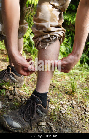 Mann gelten Beihilfen Gips am Bein. Bein mit einem Pflaster für Wunden, Mann bietet erste-Hilfe selbst. Wunde mit Pflaster versiegelt. Mann hat im Freien sein Bein kratzte. Stockfoto