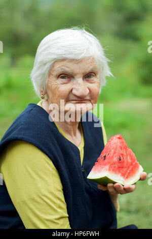 Glücklich Seniorin Essen Wassermelonen im Garten Stockfoto