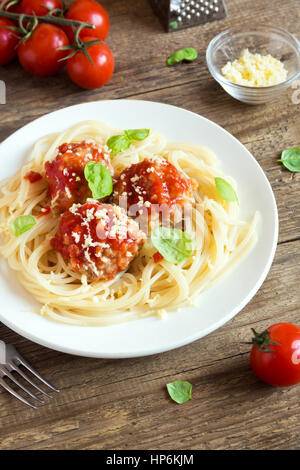 Spaghetti Nudeln mit Fleischbällchen, Tomatensauce, geriebenem Parmesan und frischem Basilikum - gesunde hausgemachte italienische Pasta auf rustikalen hölzernen Hintergrund mit Stockfoto
