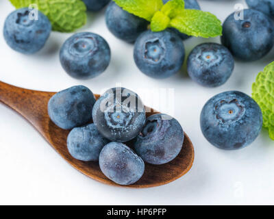 Frisch gepflückten Heidelbeeren in Holzlöffel Nahaufnahme. Reif und saftig frische Heidelbeeren mit grüner Minze auf weißem Hintergrund. Heidelbeere Antioxidans. Stockfoto