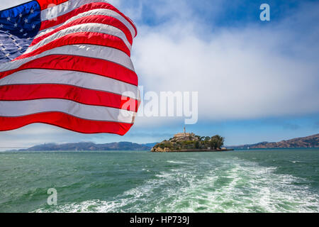 Alcatraz-Insel in der Bucht von San Francisco Skyline, Kalifornien, USA. Meerblick vom Boot nach Alcatraz mit amerikanische Flagge winken. Freiheit und Reisen Stockfoto