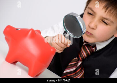 Model Release, Kleiner Geschaeftsmann, 8, Betrachtet Sparschwein Durch sterben Lupe - kleine Businesman beobachten Piggy Bank unter der Lupe Stockfoto